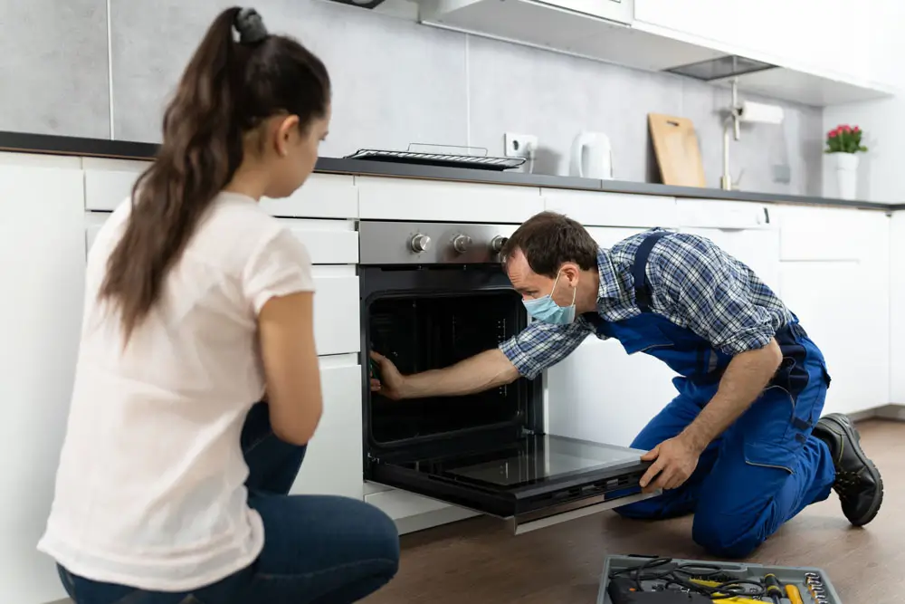 A maintenance technician repairing an oven in a rental home kitchen